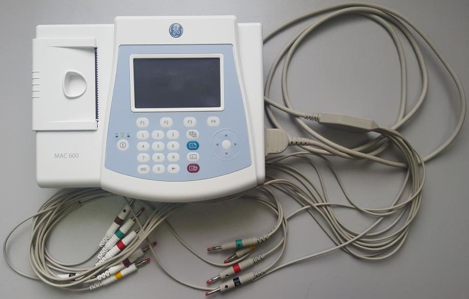 A medical electrocardiogram (ECG) machine with multiple connected leads on a gray surface.