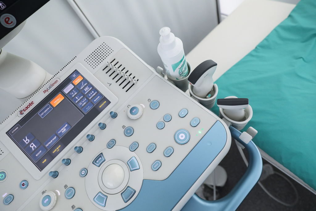 A close-up view of medical equipment used for ultrasound imaging next to an examination table.